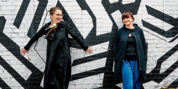 Zwei Frauen stehen lachend vor einer schwarz-weiß besprühten Wand