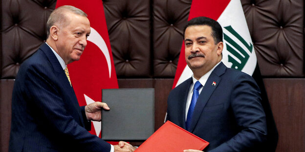 Erdogan und iraks Premierminister, beiden im blauen Anzug tauschen Dokumente aus, die in einer schwarzen und roten Mappe liegen