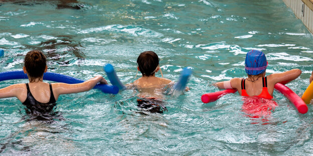 Three children side by side with a noodle in the pool