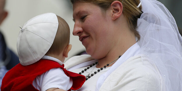 Eine Frischvermählte mit Baby auf dem Petersplatz. Papst Franziskus hat dem Kind sein Käppchen aufgesetzt. Eine Frischvermählte mit Baby auf dem Petersplatz. Papst Franziskus hat dem Kind sein Käppchen aufgesetzt.