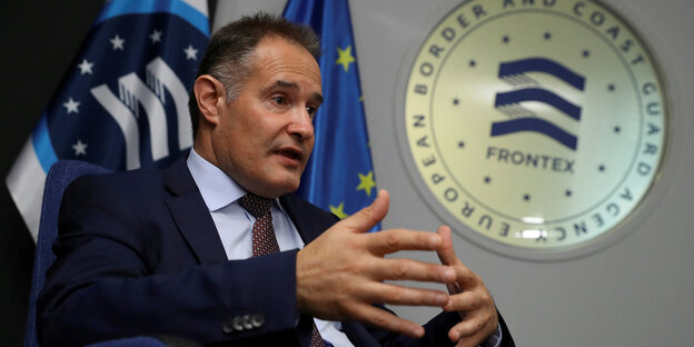 Portrait of Fabrice Leggeri, sitting in an armchair and talking, with the Frontex logo behind him.