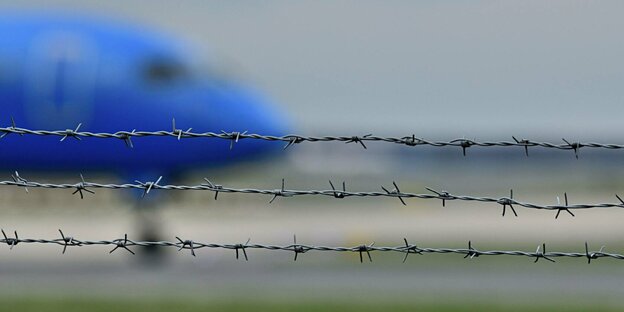 A plane arrives on the runway behind barbed wire.