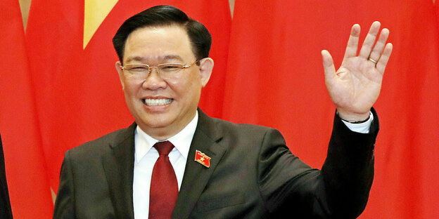 A man waves against a red background.