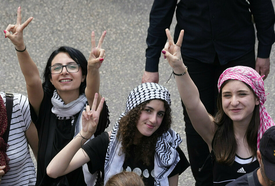 Three young women wear Pali cloths and make the victory sign.