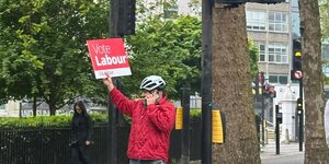 Eine Person mit Helm hält ein Schild hoch worauf steht: Vote Labor