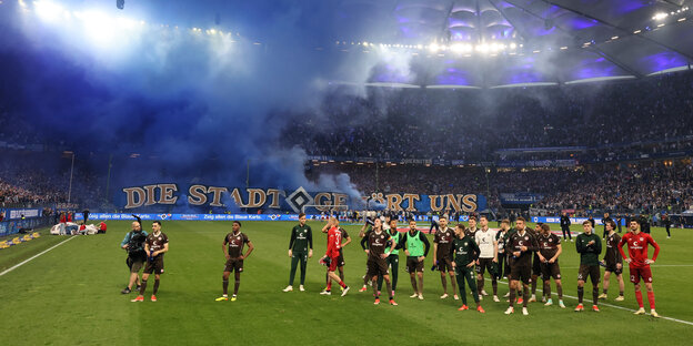 Spieler des Fc St. Pauli stehen nach dem Spiel auf dem Rasen, im Hintergrund feiern die HSV-Fans