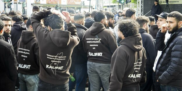 Bearded young men wear hoodies with the demand for a caliphate on the back.