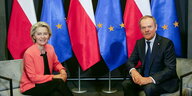 Eine Frau und ein Mann sitzen vor polnischen und europäischen Flaggen.