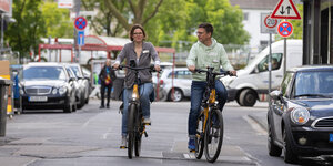 Zwei Menschen fahren mit E-Bikes durch den Kölner Stadtverkehr.
