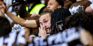 Ein Mann in einer Menge von Fußballfans wischt sich eine Träne aus dem Auge.