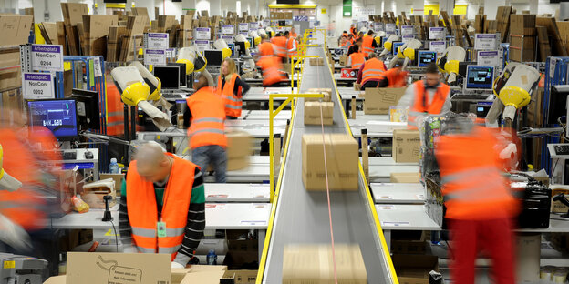 Mitarbeiter einer Amazon-Versandabteilung packen Pakete. Mitarbeiter einer Amazon-Versandabteilung packen Pakete.