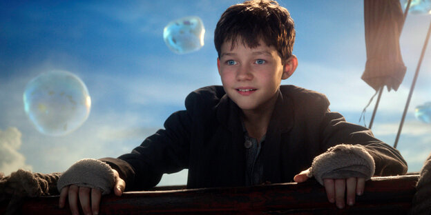 Levi Miller als Peter Pan steht an der Reling und staunt über vorbeischwebende Blasen Levi Miller als Peter Pan steht an der Reling und staunt über vorbeischwebende Blasen