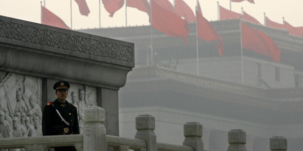 Ein Offizier steht auf einem Balkon eines Nachtbargebäudes des Nationalen Volkskongress Chinas. Im Hintergrund ist das Gebäude des Volkskongresses zu sehen, mit etlichen chinesischen Flaggen, die vom Smog vernebelt sind. Ein Offizier steht auf einem Balkon eines Nachtbargebäudes des Nationalen Volkskongress Chinas. Im Hintergrund ist das Gebäude des Volkskongresses zu sehen, mit etlichen chinesischen Flaggen, die vom Smog vernebelt sind.