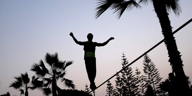 Ein Mann balanciert auf einer Slackline, nur seine Silhouette ist zu erkennen. Ein Mann balanciert auf einer Slackline, nur seine Silhouette ist zu erkennen.