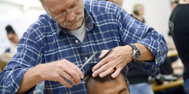 Mann im karierten Hemd schneidet anderem Mann die Haare Mann im karierten Hemd schneidet anderem Mann die Haare