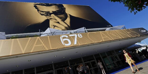 Menschen laufen an einer großen Leinwand vorbei, die auf das Cannes-Festival hinweist. Menschen laufen an einer großen Leinwand vorbei, die auf das Cannes-Festival hinweist.