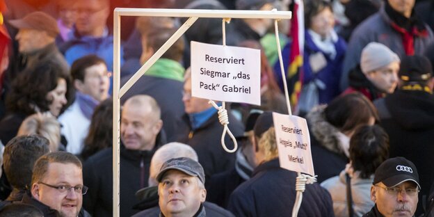 Menschen nebeneinander, irgendwer hält einen Galgen, an dem zwei Schilder hängen, dass dieser für Angela Merkel und Sigmar Gabriel gedacht ist Menschen nebeneinander, irgendwer hält einen Galgen, an dem zwei Schilder hängen, dass dieser für Angela Merkel und Sigmar Gabriel gedacht ist