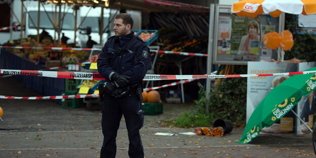 Ein Polizist auf einem Wochenmarkt. Im Hintergrund Absperrungen. Ein Polizist auf einem Wochenmarkt. Im Hintergrund Absperrungen.