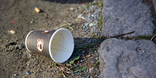 Ein leerer Kaffeebecher aus Papier liegt auf dem Boden Ein leerer Kaffeebecher aus Papier liegt auf dem Boden
