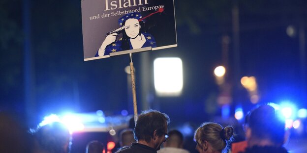 Menschen halten ein Schild auf einer Demo in die Luft.