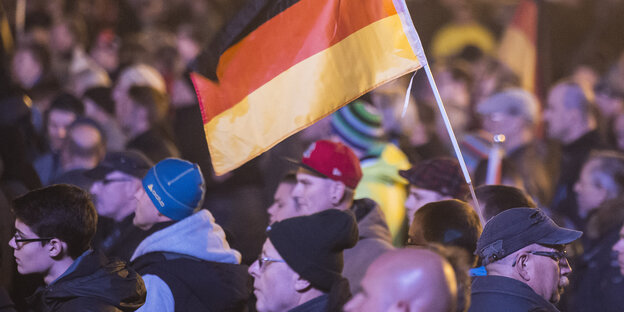 Pegida-Anhänger mit einer Deutschlandfahne in einer Menschenmenge. Pegida-Anhänger mit einer Deutschlandfahne in einer Menschenmenge.