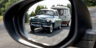 Im Rückspiegel eines Autos ist ein altes Auto mit Wohwagenanhänger zu sehen