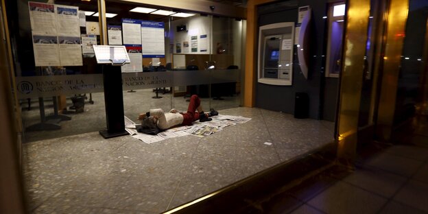 Ein Mann liegt auf dem Boden im Vorraum einer Bank und schläft Ein Mann liegt auf dem Boden im Vorraum einer Bank und schläft