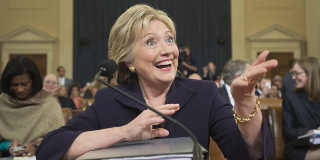 Hillary Clinton lacht, vor ihr liegt ein Aktenordner Hillary Clinton lacht, vor ihr liegt ein Aktenordner