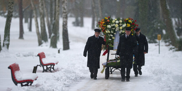 Friedhofsmitarbeiter bringen Blumenkränze zu einem Grab Friedhofsmitarbeiter bringen Blumenkränze zu einem Grab