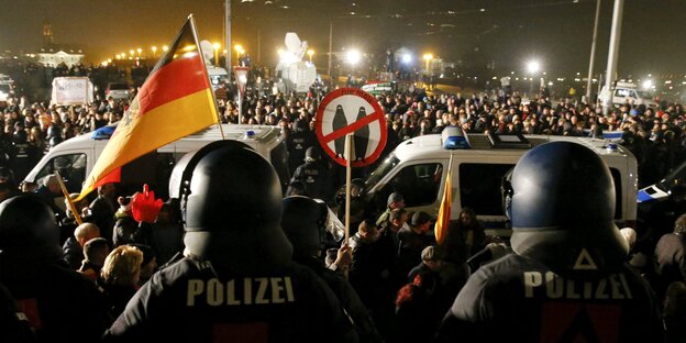 Polizisten in Kampfmontur, dahinter Demonstraten mit Deutschlandfahne