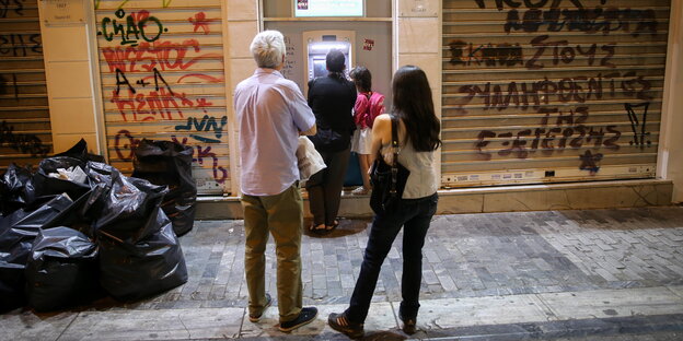 Menschen stehen Schlange vor einem Bankautomaten in Athen Menschen stehen Schlange vor einem Bankautomaten in Athen