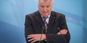 Horst Seehofer steht vor blauem Hintergrund und blickt nach unten