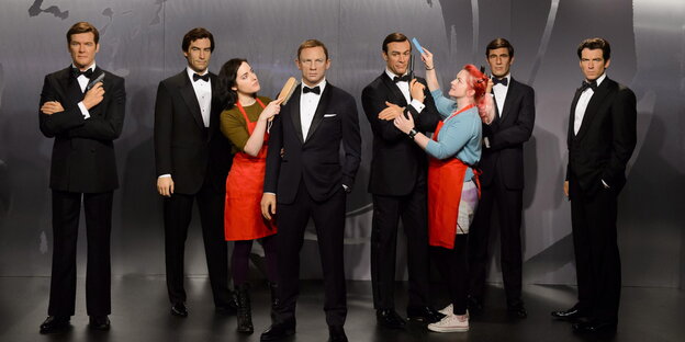 Zwei Frauen inmitten von aktuelle und früheren James-Bond-Darstellter als Wachsfiguren Zwei Frauen inmitten von aktuelle und früheren James-Bond-Darstellter als Wachsfiguren