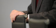 John Cryan legt vor dem Logo der Deutschen Bank eine Hand auf die Stuhllehne