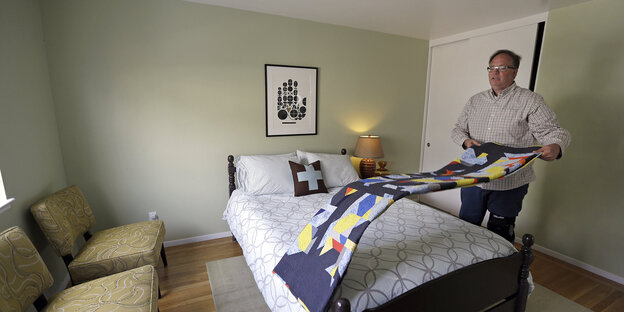 Ein Airbnb-Gastgeber macht die Betten in dem Zimmer, das er und sein Ehemann untervermieten Ein Airbnb-Gastgeber macht die Betten in dem Zimmer, das er und sein Ehemann untervermieten