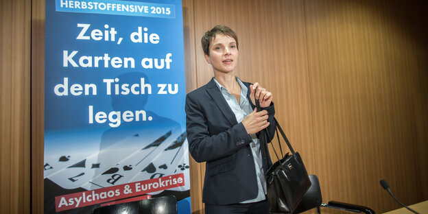 AfD-Parteivorsitzende steht vor einem Kampagnenplakat