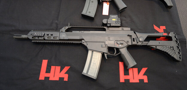Ein G36-Geweher liegt auf schwarzem Boden, daneben steht mehrfach „HK“ Ein G36-Geweher liegt auf schwarzem Boden, daneben steht mehrfach „HK“