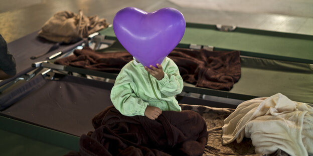 Ein Kind in einer Flüchtlingsunterkunft in Graz hält sich einen lila Luftballon in Herzform vor das Gesicht. Ein Kind in einer Flüchtlingsunterkunft in Graz hält sich einen lila Luftballon in Herzform vor das Gesicht.