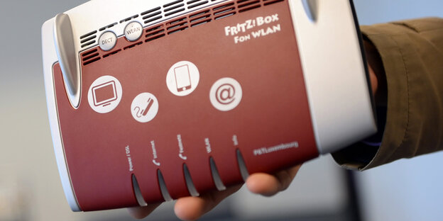 Eine Hand hält einen bordeauxfarbenen Router. Eine Hand hält einen bordeauxfarbenen Router.