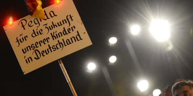 Ein Schild mit einem Spruch, darüber hängt eine Deutschlandflagge. Es ist dunkel. Im Hintergrund sind Lichter. Ein Schild mit einem Spruch, darüber hängt eine Deutschlandflagge. Es ist dunkel. Im Hintergrund sind Lichter.
