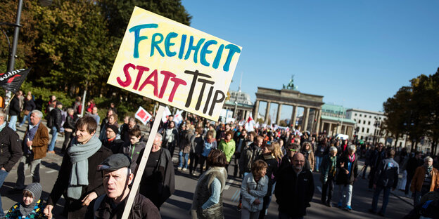 Viele Menschen auf einer Straße, einer hat ein Schild mit der Aufschrift "Freiheit statt TTIP", im Hintergrund das Brandenburger Tor (Berlin) Viele Menschen auf einer Straße, einer hat ein Schild mit der Aufschrift "Freiheit statt TTIP", im Hintergrund das Brandenburger Tor (Berlin)