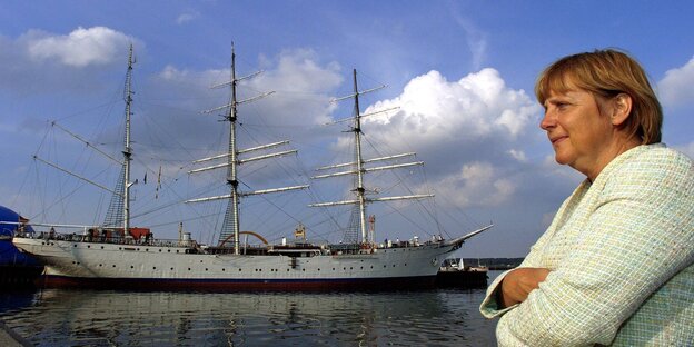 Merkel guckt grimmig, hinter ihr ein Segelschiff, es ist die Gorch Fock