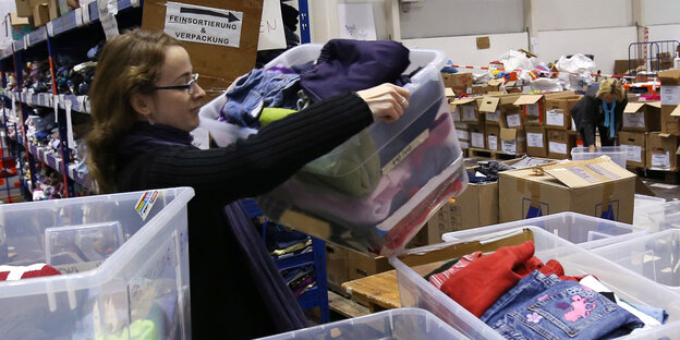 Eine Frau steht inmitten von Kisten mit gespendeter Kleidung. Sie sortiert sie. Eine Frau steht inmitten von Kisten mit gespendeter Kleidung. Sie sortiert sie.