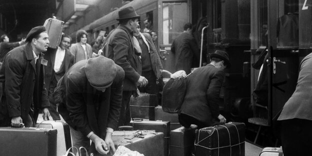 Viele Männer stehen vor einem Zug und sammeln ihre Koffer, um einzusteigen Viele Männer stehen vor einem Zug und sammeln ihre Koffer, um einzusteigen