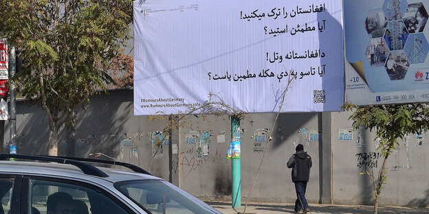 Ein Plakat mit der Aufschrift „Sie verlassen Afghanistan? Sind sie sicher?“. Davor Autos auf der Straße