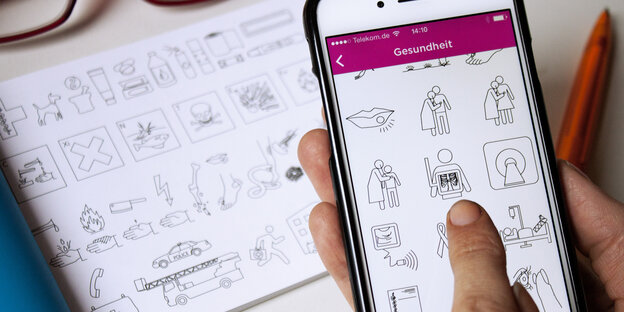 Ein Smartphone mit Bildern zu Gesundheit. Dahinter ein Buch mit anderen Bildern. Ein Smartphone mit Bildern zu Gesundheit. Dahinter ein Buch mit anderen Bildern.