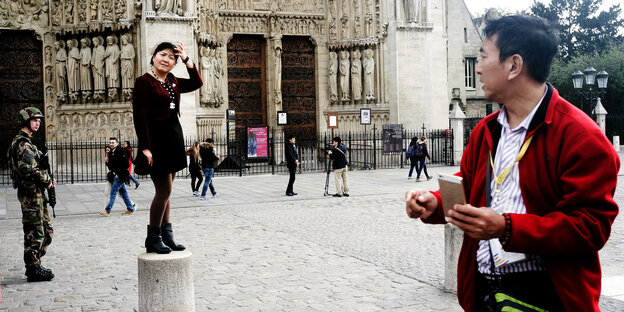 Touristen posieren vor Notre-Dame, ein Soldat schaut zu Touristen posieren vor Notre-Dame, ein Soldat schaut zu