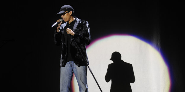 Xavier Naidoo singt auf einer Bühne, im Hintergrund ist sein Schatten zu sehen. Xavier Naidoo singt auf einer Bühne, im Hintergrund ist sein Schatten zu sehen.