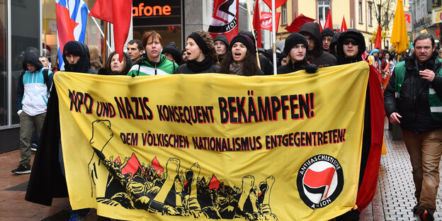 Im Vordergrund ein Banner, auf dem steht: "NPD und Nazis konsequent bekämpfen!" und weiter "Dem völkischen Nationalismus entgegentreten!". Das Banner tragen AntifaschistInnen, dahinter läuft ein bunter Demonstrationszug durch die Stadt. Im Vordergrund ein Banner, auf dem steht: "NPD und Nazis konsequent bekämpfen!" und weiter "Dem völkischen Nationalismus entgegentreten!". Das Banner tragen AntifaschistInnen, dahinter läuft ein bunter Demonstrationszug durch die Stadt.