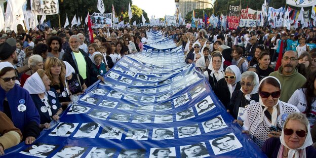 Viele Menschen auf einer Straße, die ein mehrere Meter langes Transparent tragen, auf dem Schwarz-Weiß-Fotos von Menschen sind - eine Gedenkveranstaltung für Opfer der argentinischen Militärdiktatur Viele Menschen auf einer Straße, die ein mehrere Meter langes Transparent tragen, auf dem Schwarz-Weiß-Fotos von Menschen sind - eine Gedenkveranstaltung für Opfer der argentinischen Militärdiktatur